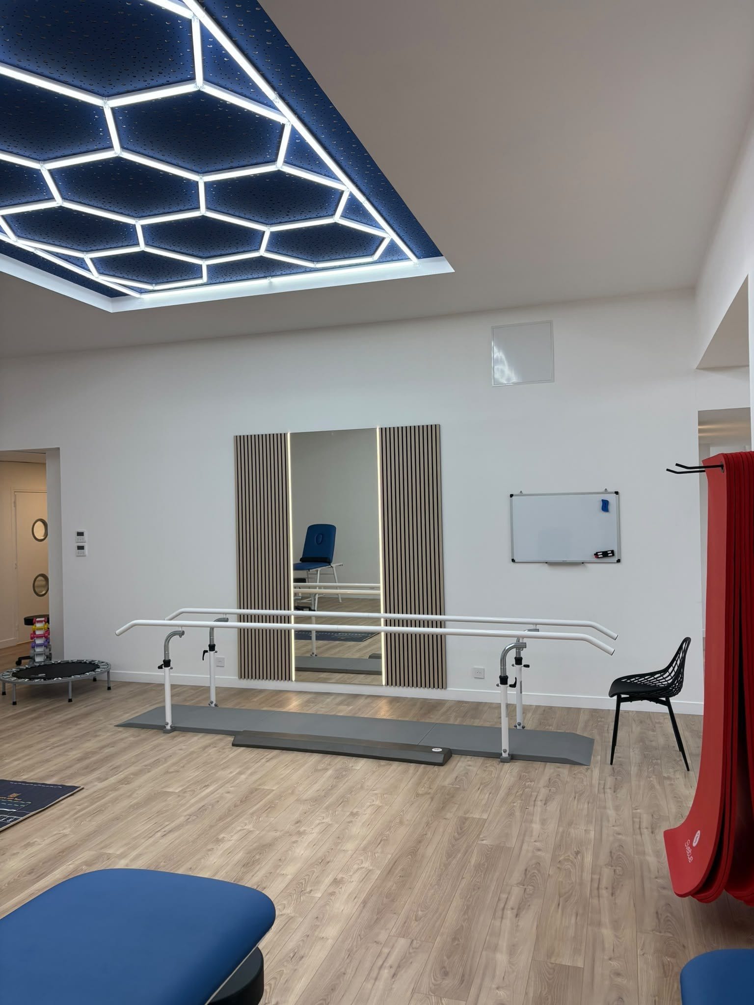 Barres parallèles de rééducation à la marche devant un miroir, sous le plafond lumineux hexagonal
